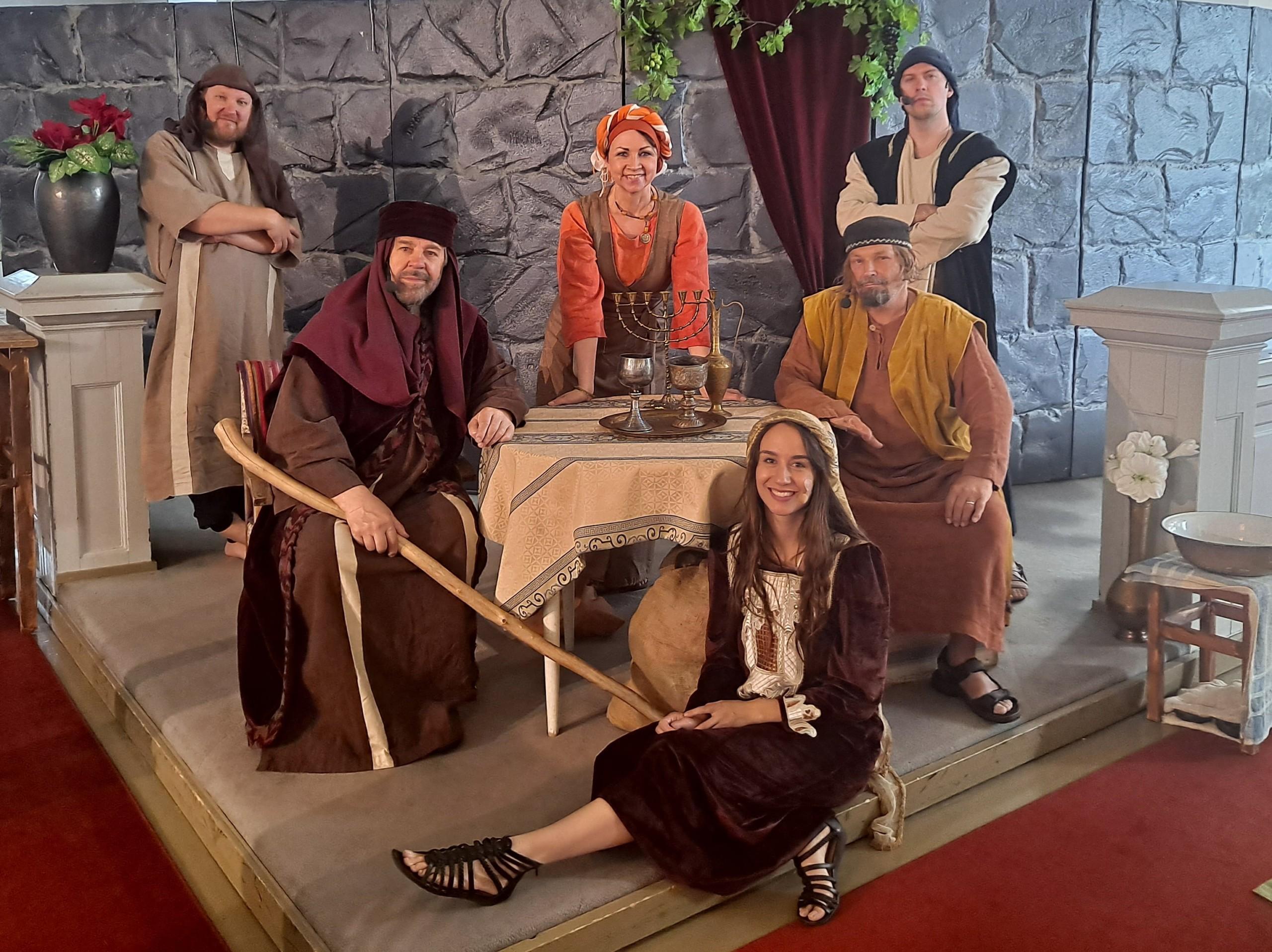6 näyttelijää lavasteiden keskellä raamatunaikaisissa roolivaatteissa. Katsovat kameraan hymyillen.